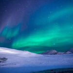 Aurora boreal de tonos verdes y violetas en una noche sobre un lugar frío y nevado. Prueba del magnetismo terrestre.