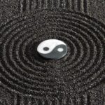 Símbolo del Yin y el Yang, básico en el Feng Shui. Está sobre arena de color negro que forma círculos concéntricos alrededor del símbolo.