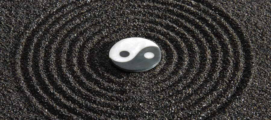 Símbolo del Yin y el Yang, básico en el Feng Shui. Está sobre arena de color negro que forma círculos concéntricos alrededor del símbolo.