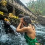Mujer joven en un ritual de purificación (Melukat) en un templo de Bali. Está dentro del agua y purificándose con agua que sale de la fuente.