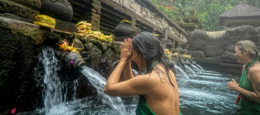 Mujer joven en un ritual de purificación (Melukat) en un templo de Bali. Está dentro del agua y purificándose con agua que sale de la fuente.