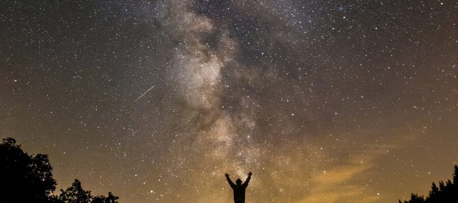 Silueta de un hombre de lejos en un campo. Es de noche y el cielo está muy claro y estrellado. Símbolo de unión entre el Cielo, la Tierra y el ser humano.