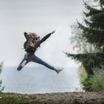 Mujer joven de espaldas en medio de la naturaleza. Se siente muy feliz y está saltando bien alto y levantando los brazos.