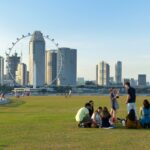 Grupo de jóvenes sentados en una zona de césped con la ciudad de Singapur de fondo. Muestra del espíritu kampong de Singapur.