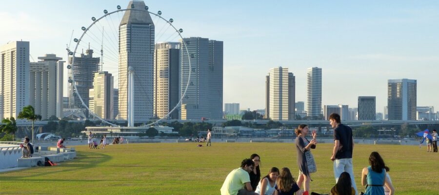 Grupo de jóvenes sentados en una zona de césped con la ciudad de Singapur de fondo. Muestra del espíritu kampong de Singapur.