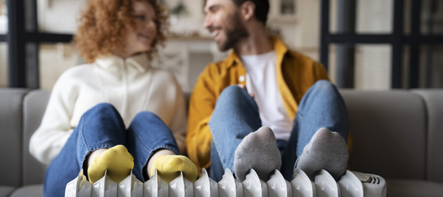 Una pareja joven sentada y reposando sus pies sobre un radiador para disfrutar de la calefacción en casa.