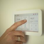 Una mano seleccionando en un termostato la temperatura ideal de la calefacción para la casa, según los criterios de biohabitabilidad para vivir en una casa sana.